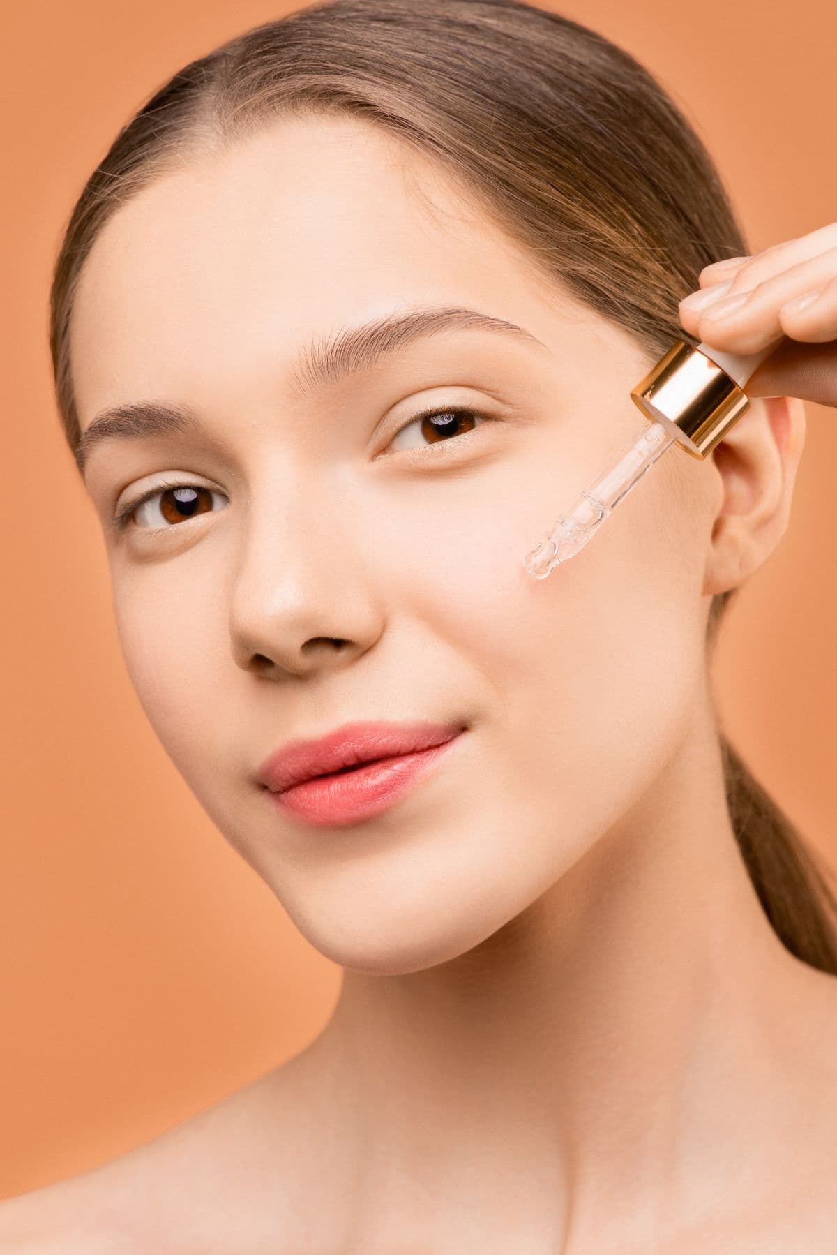 A woman applying a clear serum to her cheek with a glass dropper