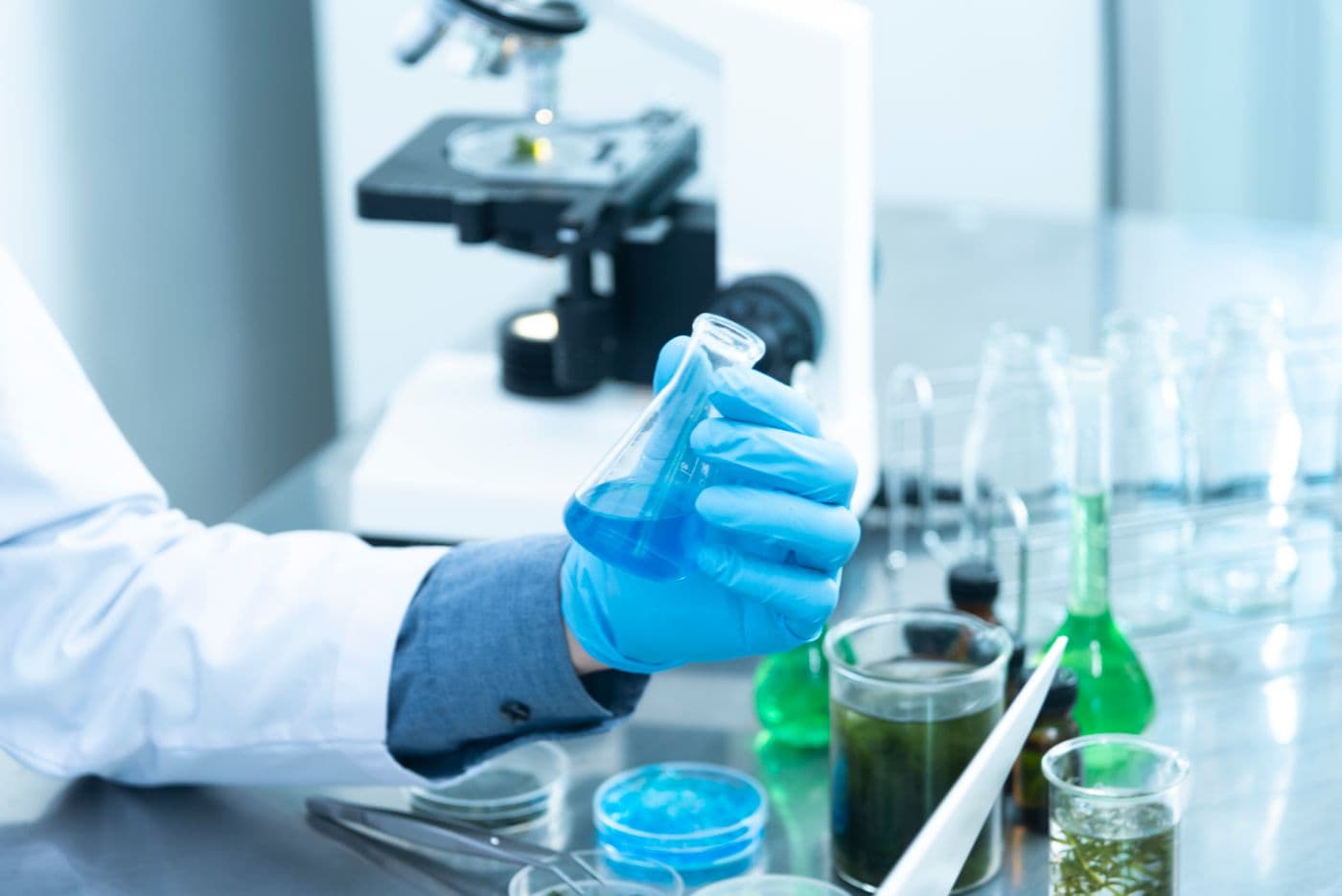 A gloved hand holding a flask in a cosmetic science lab