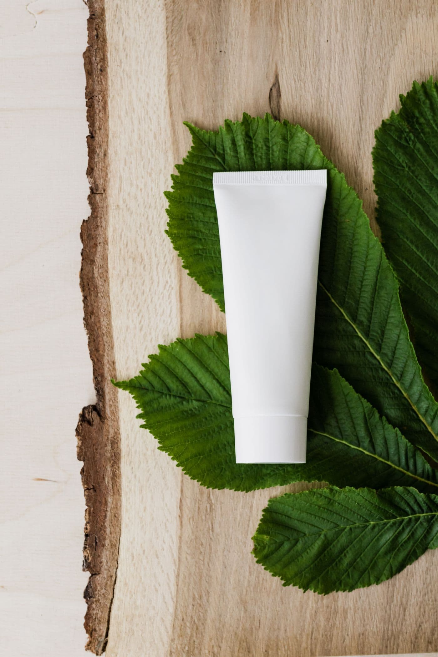 An unbranded white skincare tube resting on green leaves