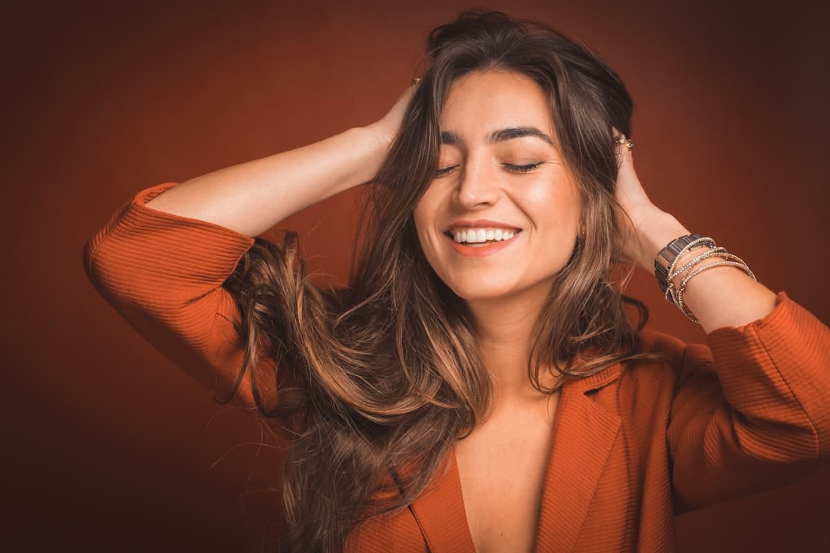 A smiling woman running both hands through her long, wavy brown hair